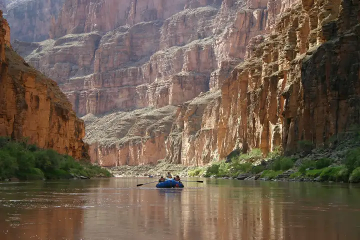 A raft on the Colorado River far below tall red canyon walls in the Grand Canyon