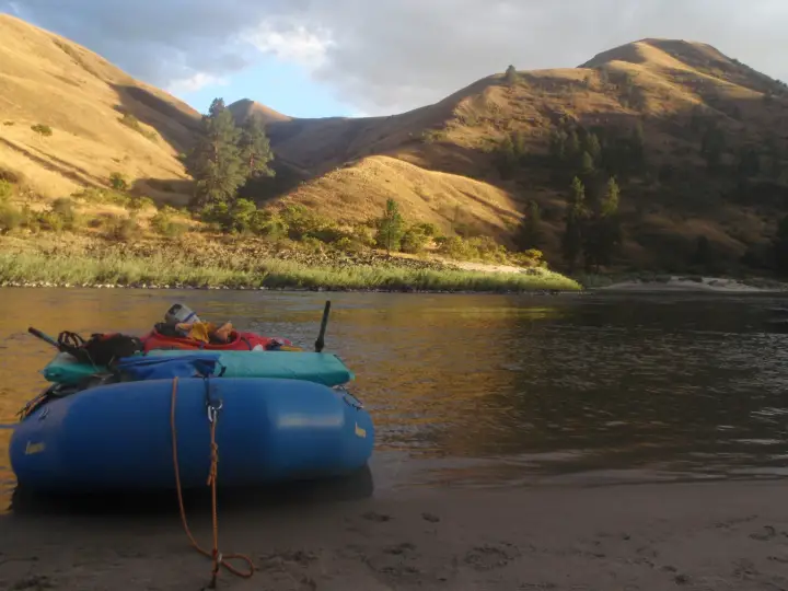 A blue raft pulled up on a sand beach on the Salmon River under golden evening light